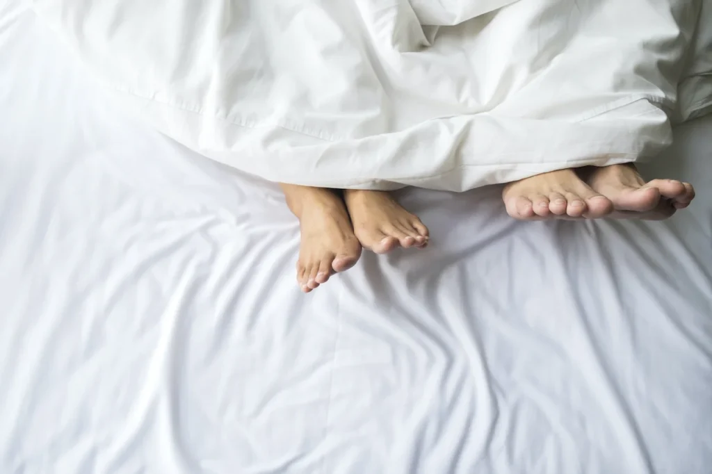 kobiece i męskie bose stopy wystają spod białej pościeli w łóżku, gdzie mogą być pluskwy
